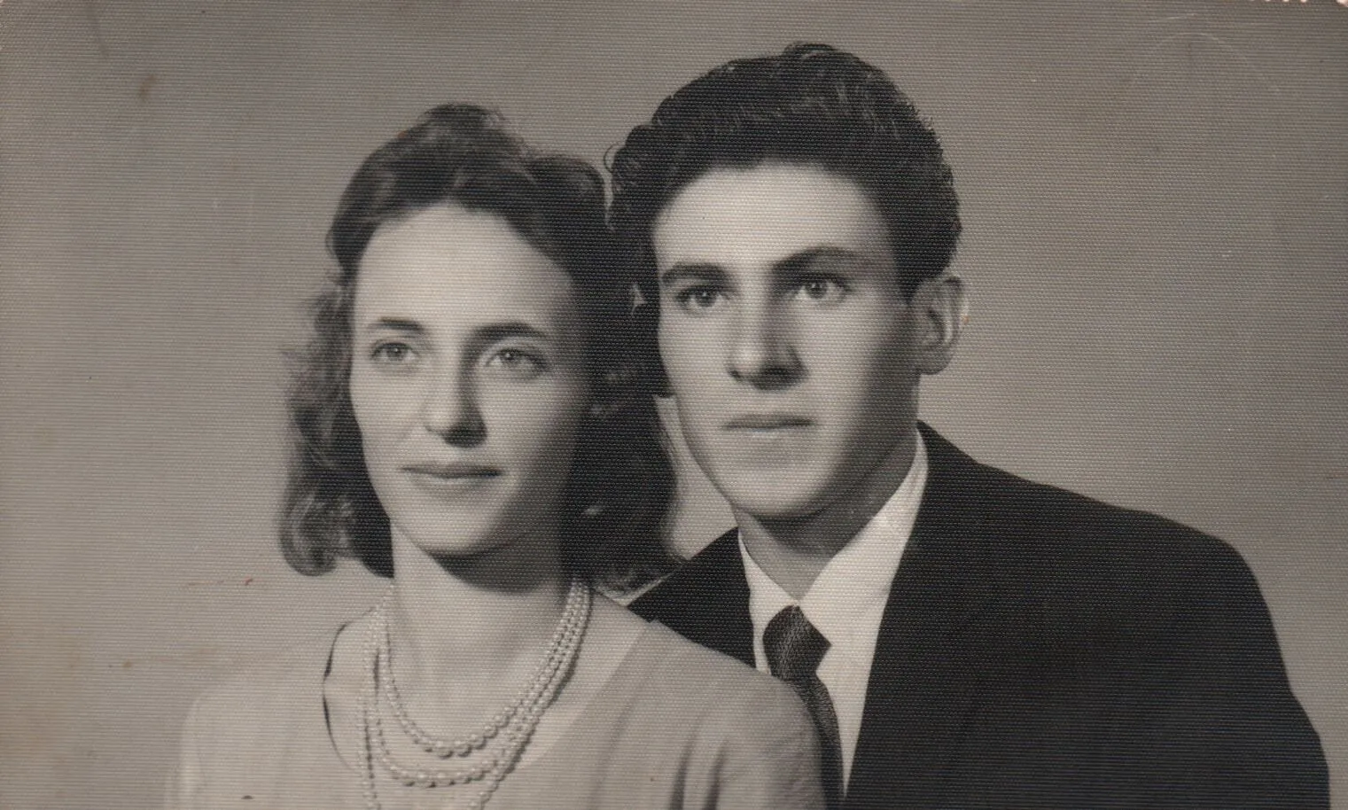 Retrato de um jovem casal de meados do século XX; a mulher em primeiro plano, usando um colar de pérolas, e o homem ligeiramente atrás dela, ambos olhando para a frente. (Original)