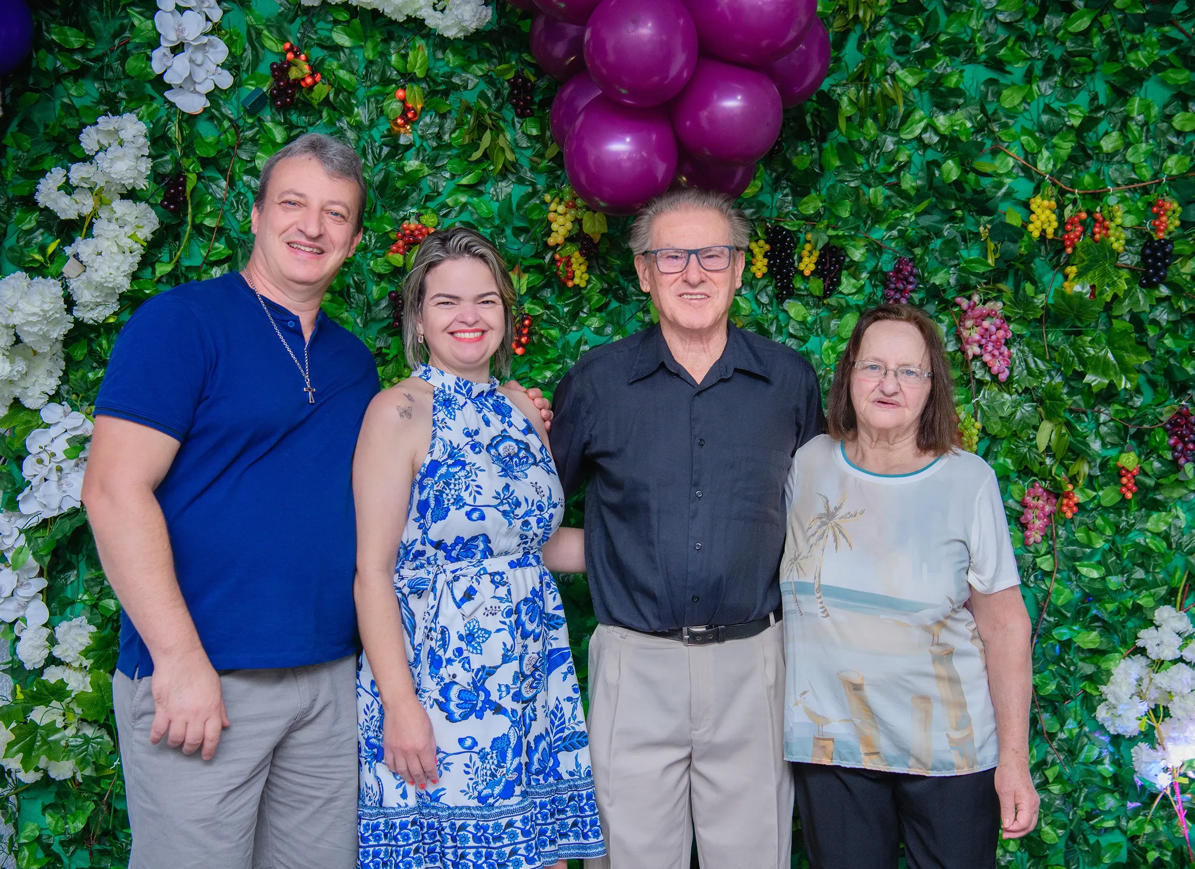 Duas mulheres e dois homens sorrindo para a câmera, em frente a um jardim vertical decorado com uvas roxas e balões.