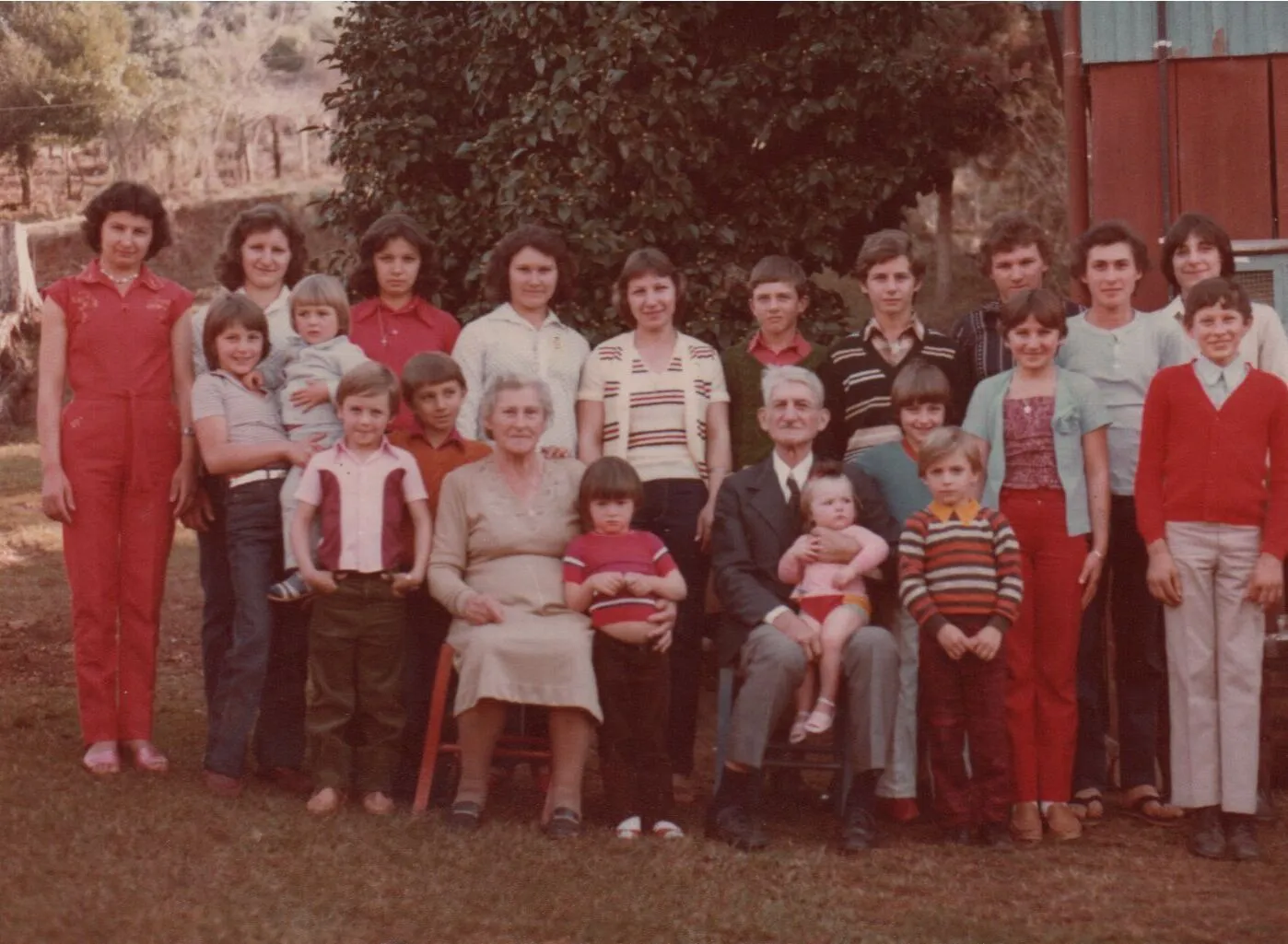 Um grupo grande e multigênero posa para uma foto de família ao ar livre, com a maioria dos membros do grupo sorrindo. (Original)