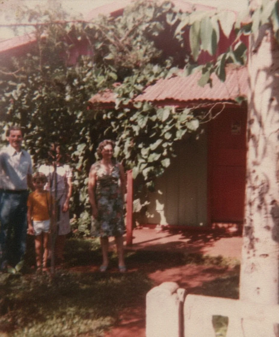 Fotografia granulada de uma família de quatro pessoas em frente a uma casa de campo coberta de vinhas.