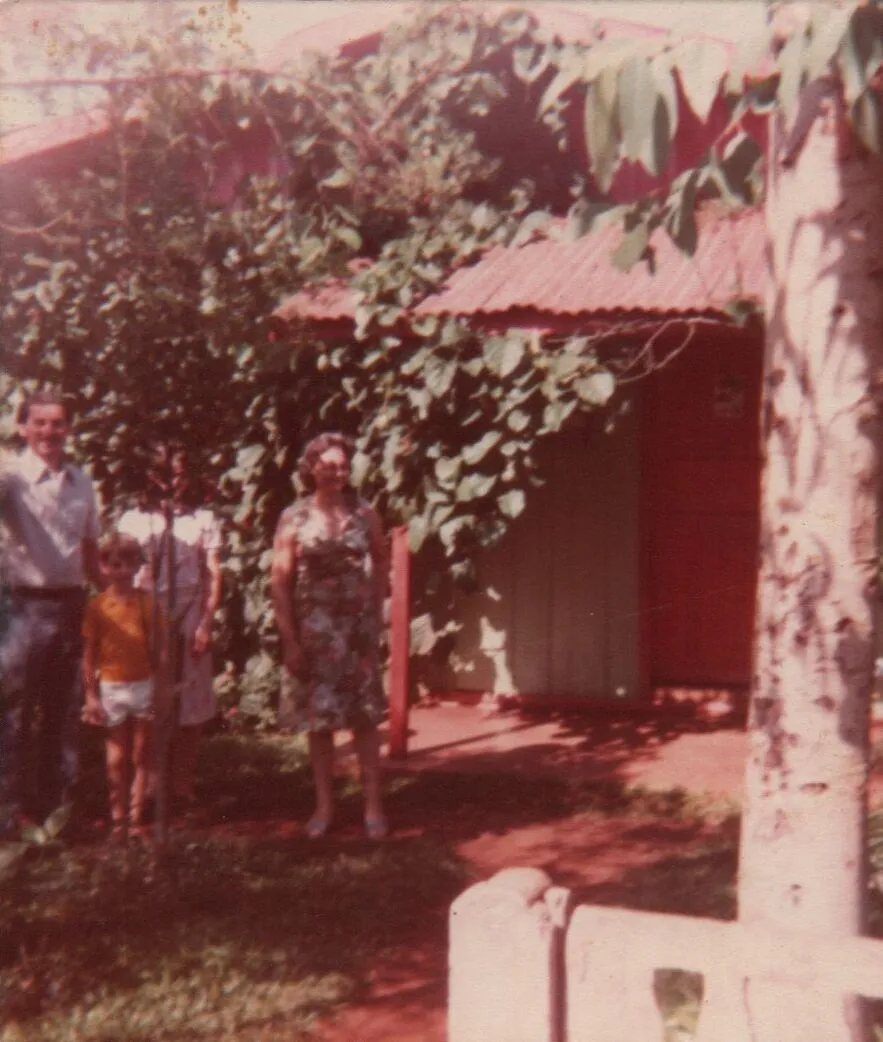 Fotografia granulada de uma família de quatro pessoas em frente a uma casa de campo coberta de vinhas. (Original)