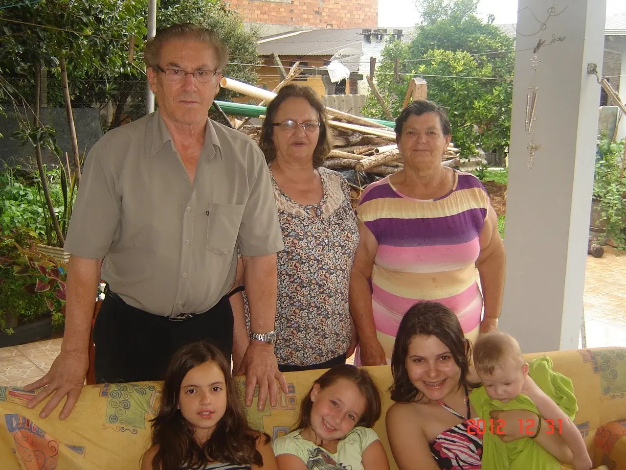 Sete pessoas de diferentes idades posam para a câmera, com as quatro pessoas mais velhas em pé atrás do sofá e as três crianças sentadas à frente, no sofá.