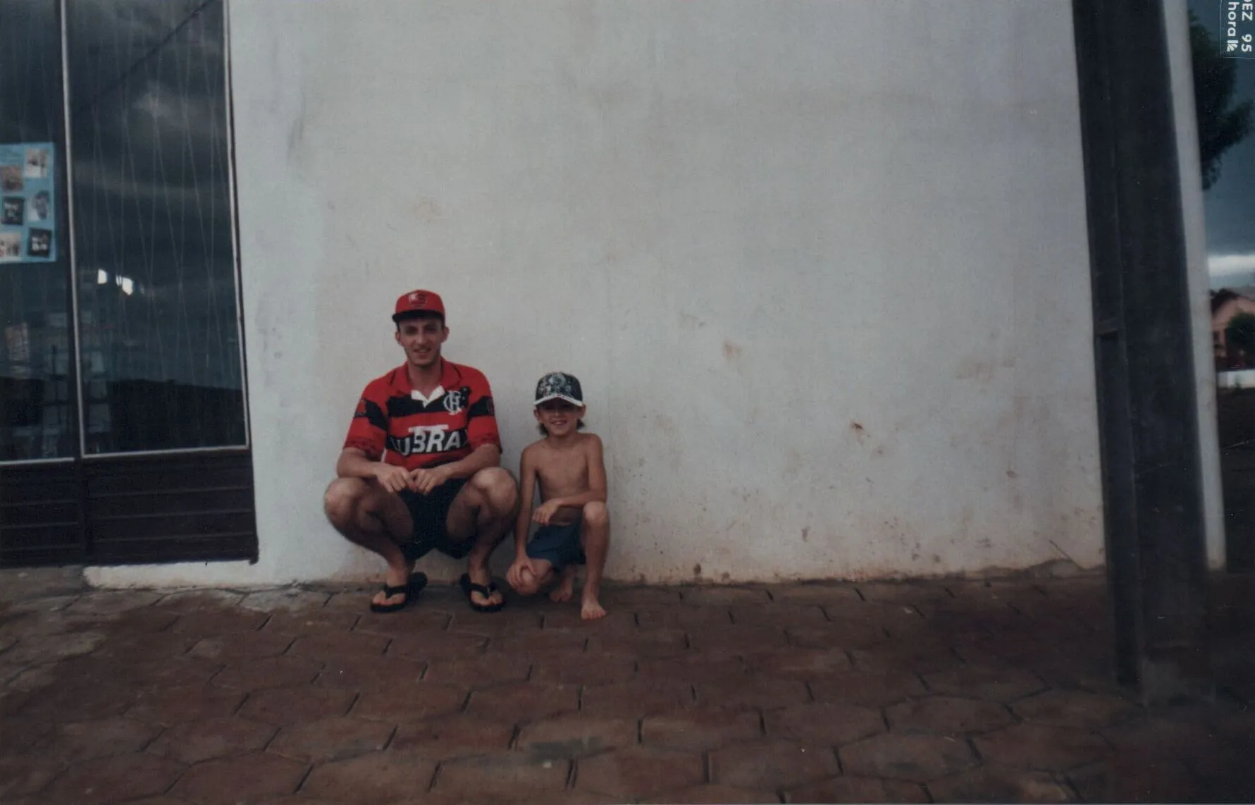 Um homem e um menino agachados contra uma parede branca.