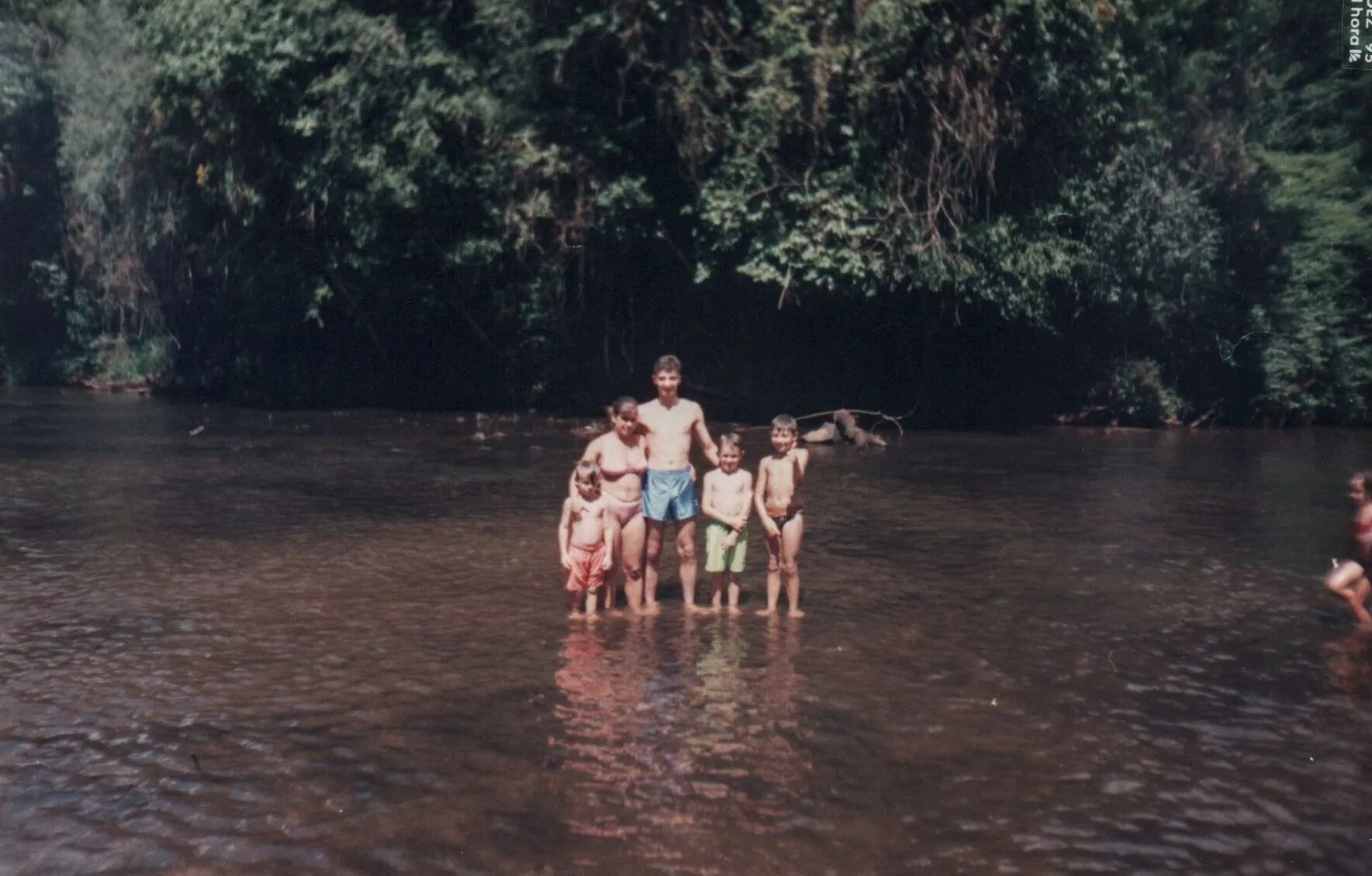 Um grupo de cinco crianças e dois adultos em pé na água em uma área arborizada.