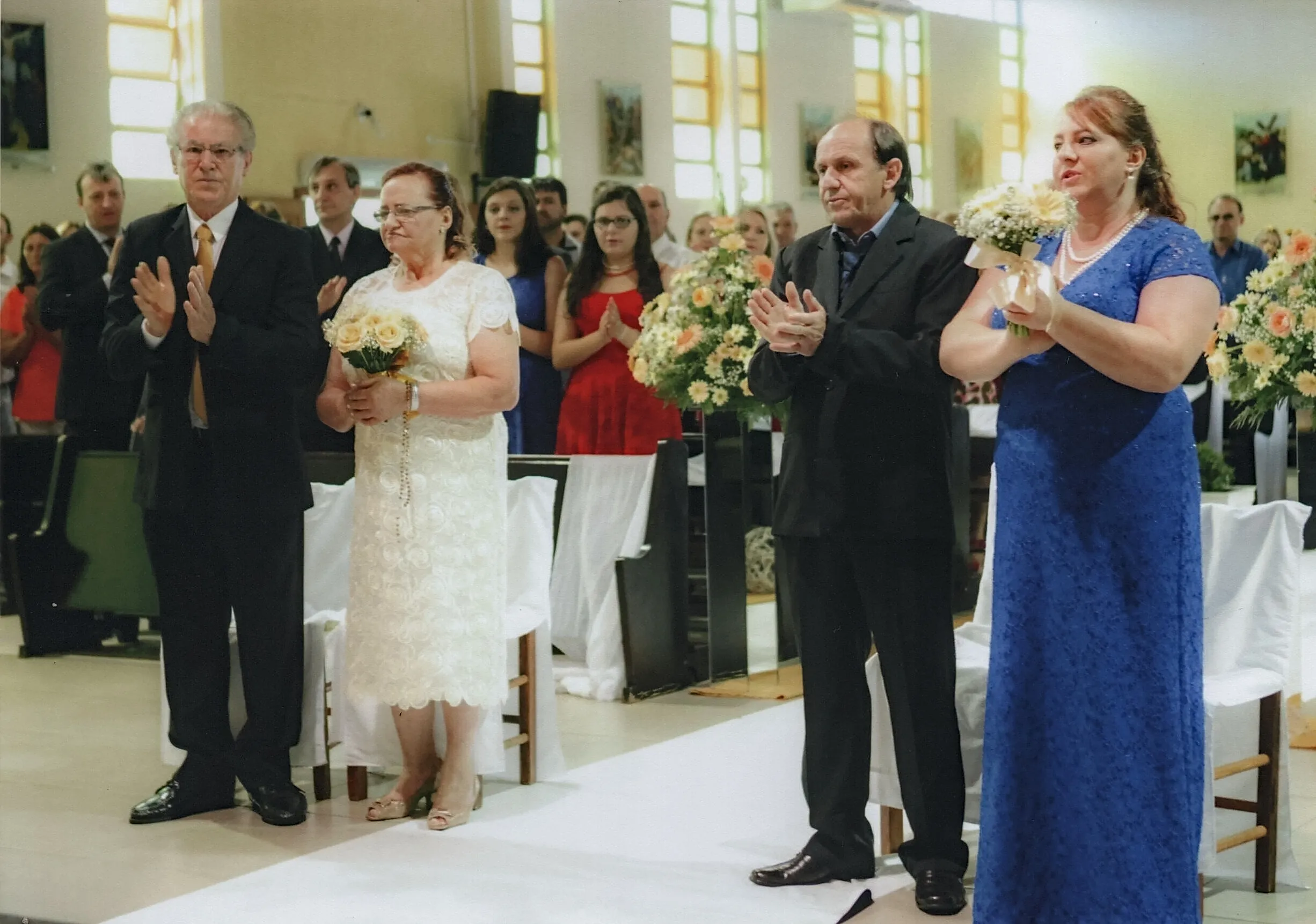 Quatro convidados de casamento, dois homens e duas mulheres, estão em pé na nave da igreja aplaudindo.