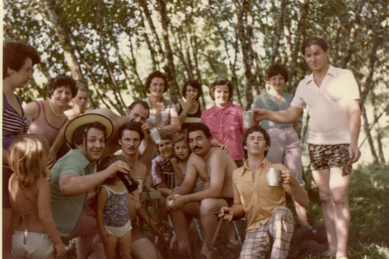 Um grupo de vinte pessoas de várias idades está posando para uma foto ao ar livre.