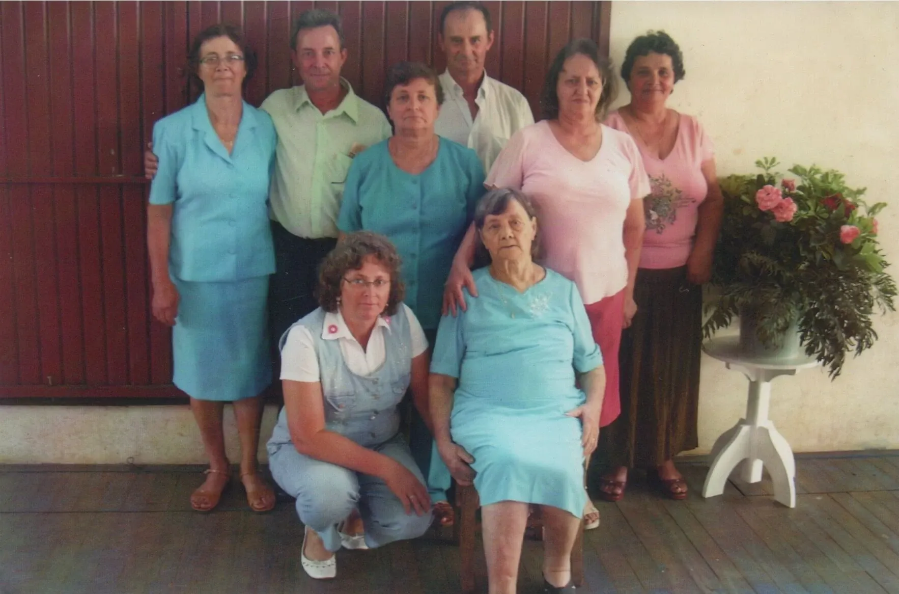 Oito adultos posam para uma foto em um quarto com paredes marrons.