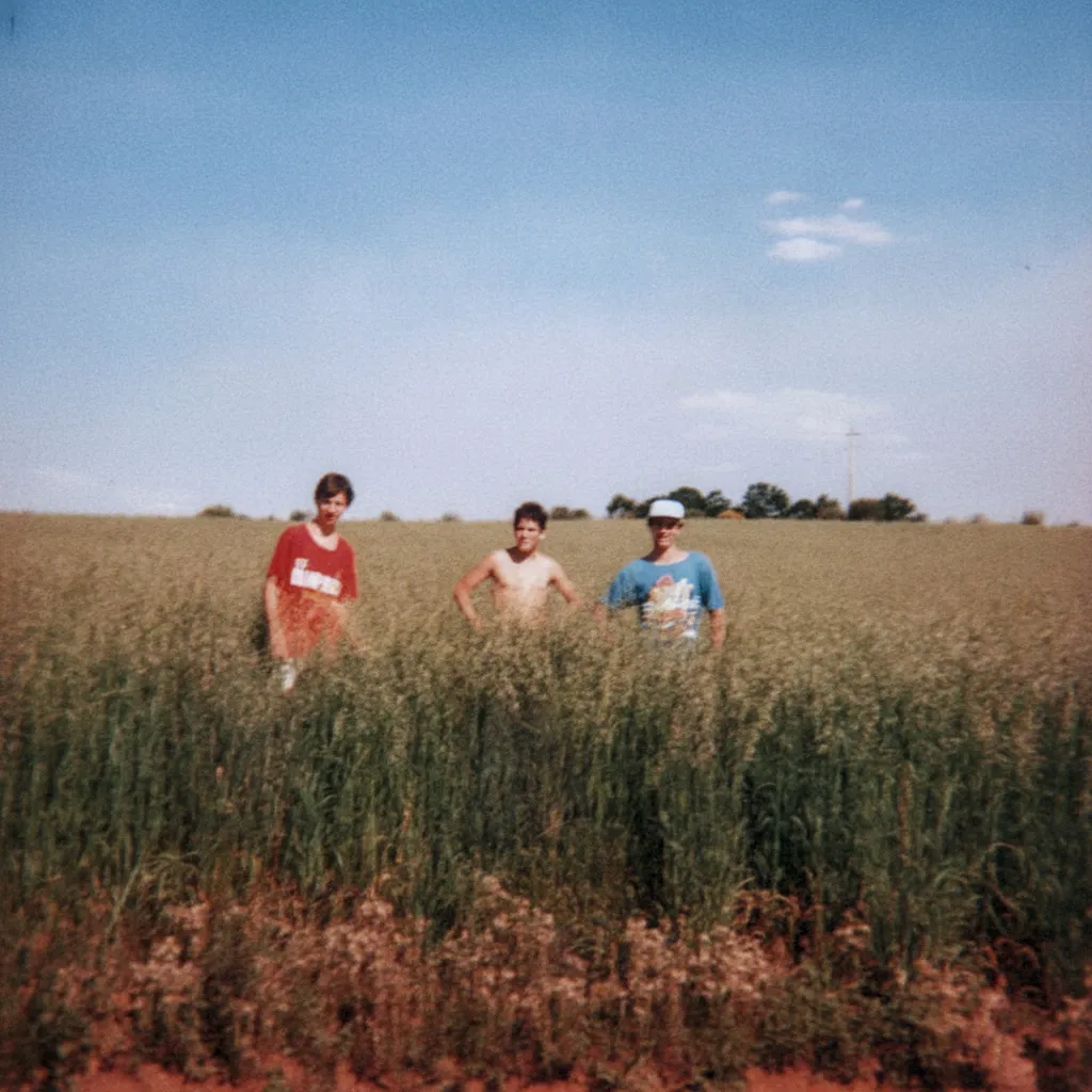 Três meninos posam em um campo verde sob um céu azul claro.