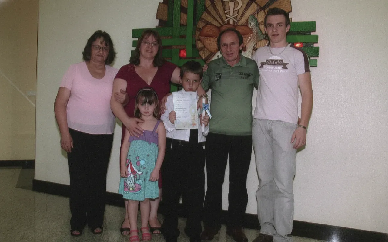 Um grupo de seis pessoas, incluindo duas mulheres, dois homens e duas crianças, posa para uma foto em pé na frente de uma decoração de parede.