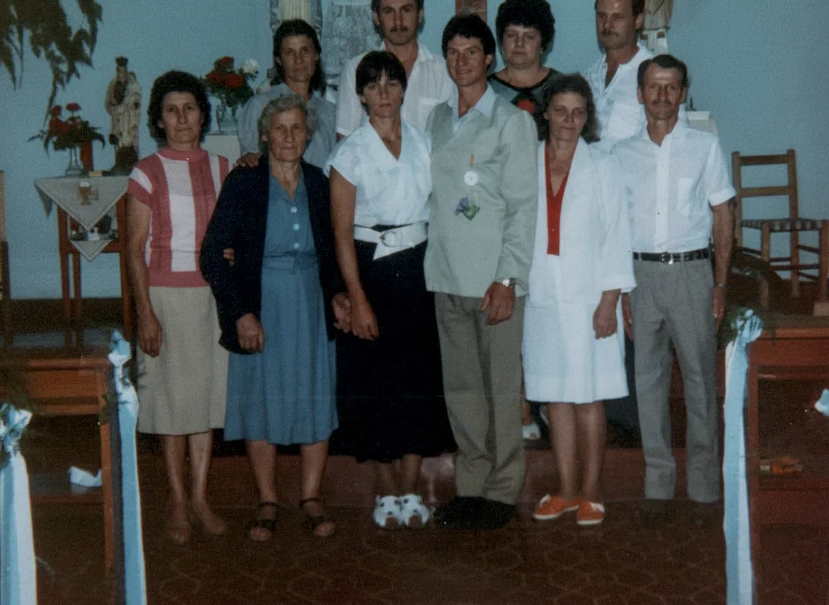 Uma fotografia envelhecida de um grande grupo de nove adultos, com seis mulheres e três homens, posando juntos num salão de reuniões com decoração de estilo igreja.
