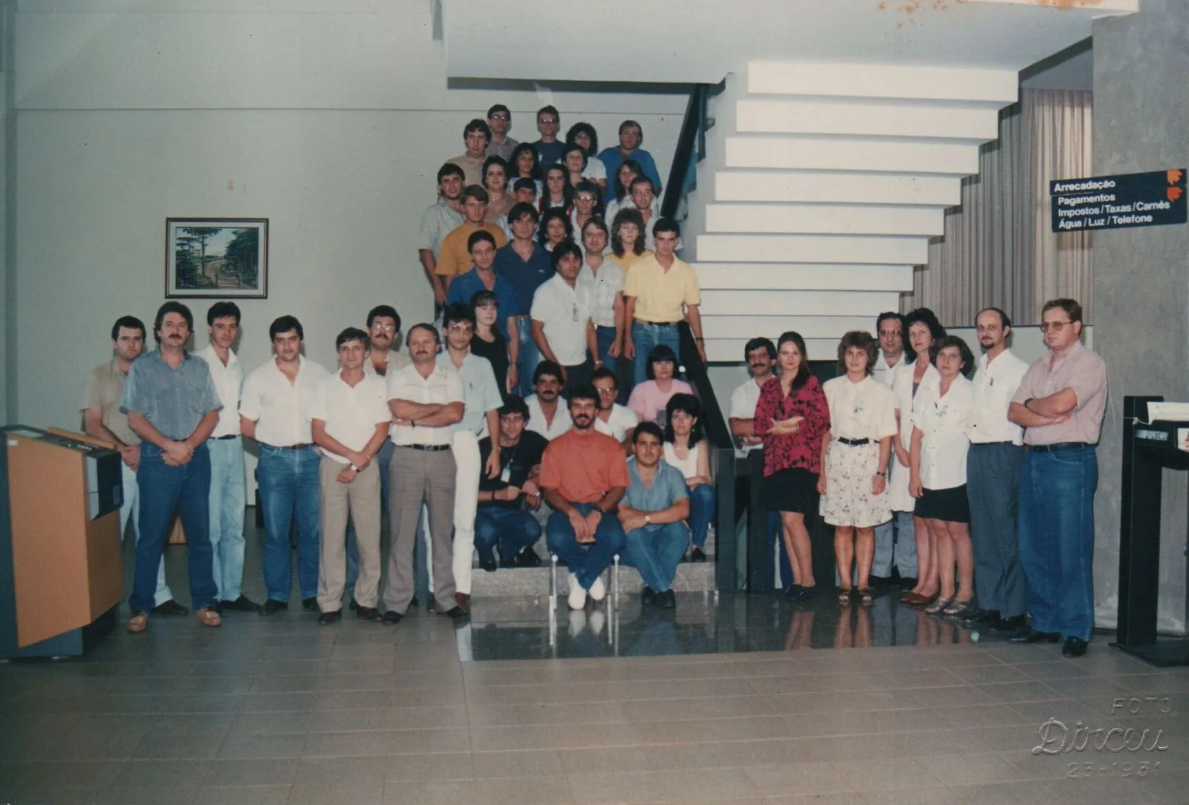 Grupo de cerca de 30 a 40 pessoas, maioritariamente homens, posa em escadas e chão interior, com alguns em pé e sentados na frente. (Original)