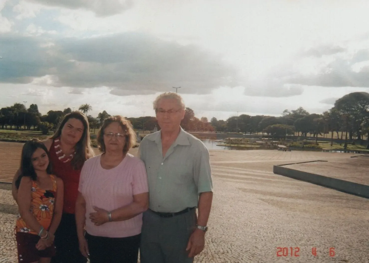 Uma família de quatro pessoas — uma jovem, uma adolescente, uma mulher de meia-idade e um homem mais velho — posa para uma foto ao ar livre.