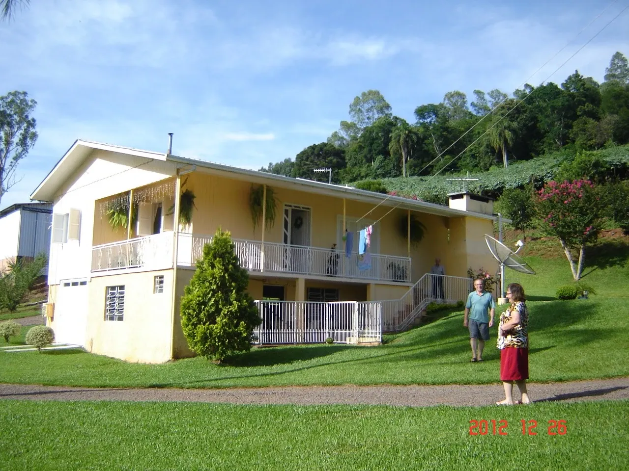 Duas pessoas de pé em um gramado em frente a uma casa de dois andares com varanda.