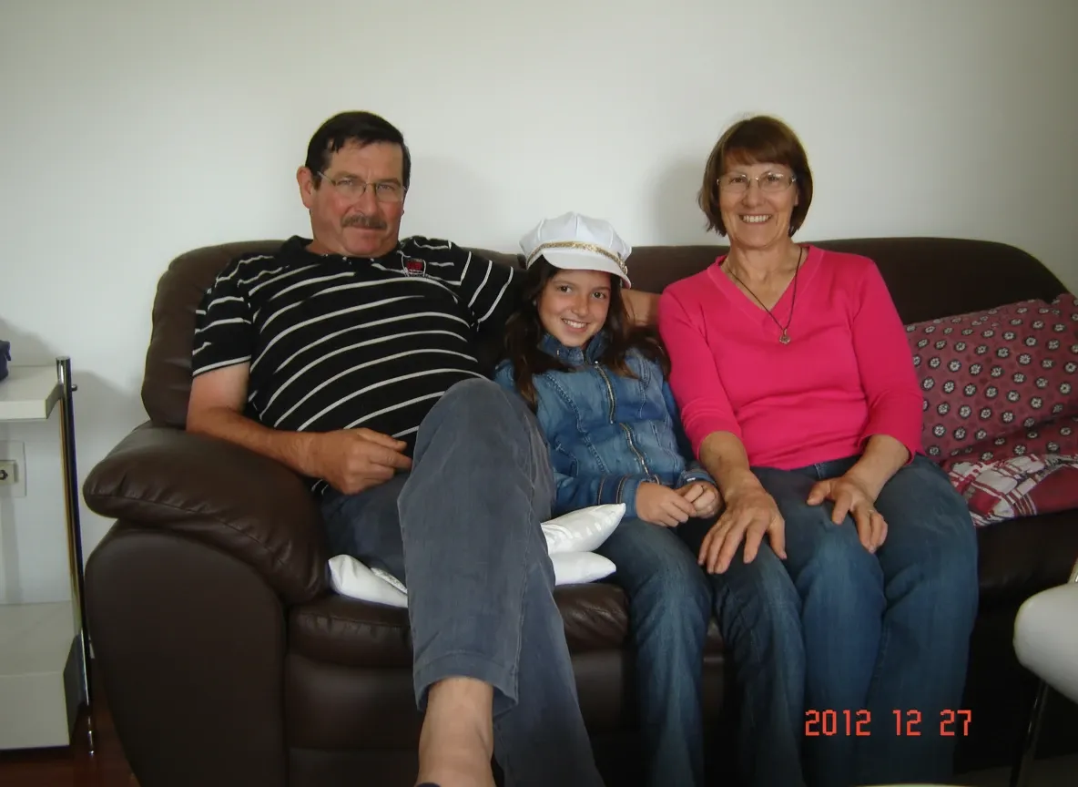 Avós e neta sentados juntos num sofá castanho.