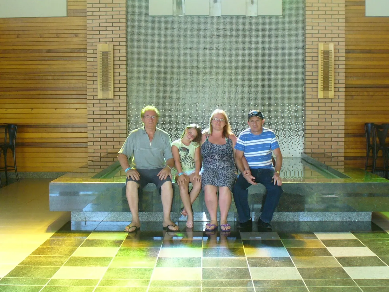 Quatro pessoas, duas mulheres e dois homens de diferentes idades, sentados em um banco de pedra em um hotel, posando para a câmera.