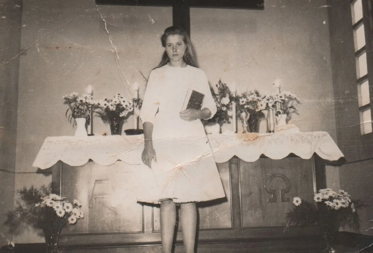 Jovem em um vestido branco segurando um livro em frente a um altar decorado com velas e flores brancas. (Original)
