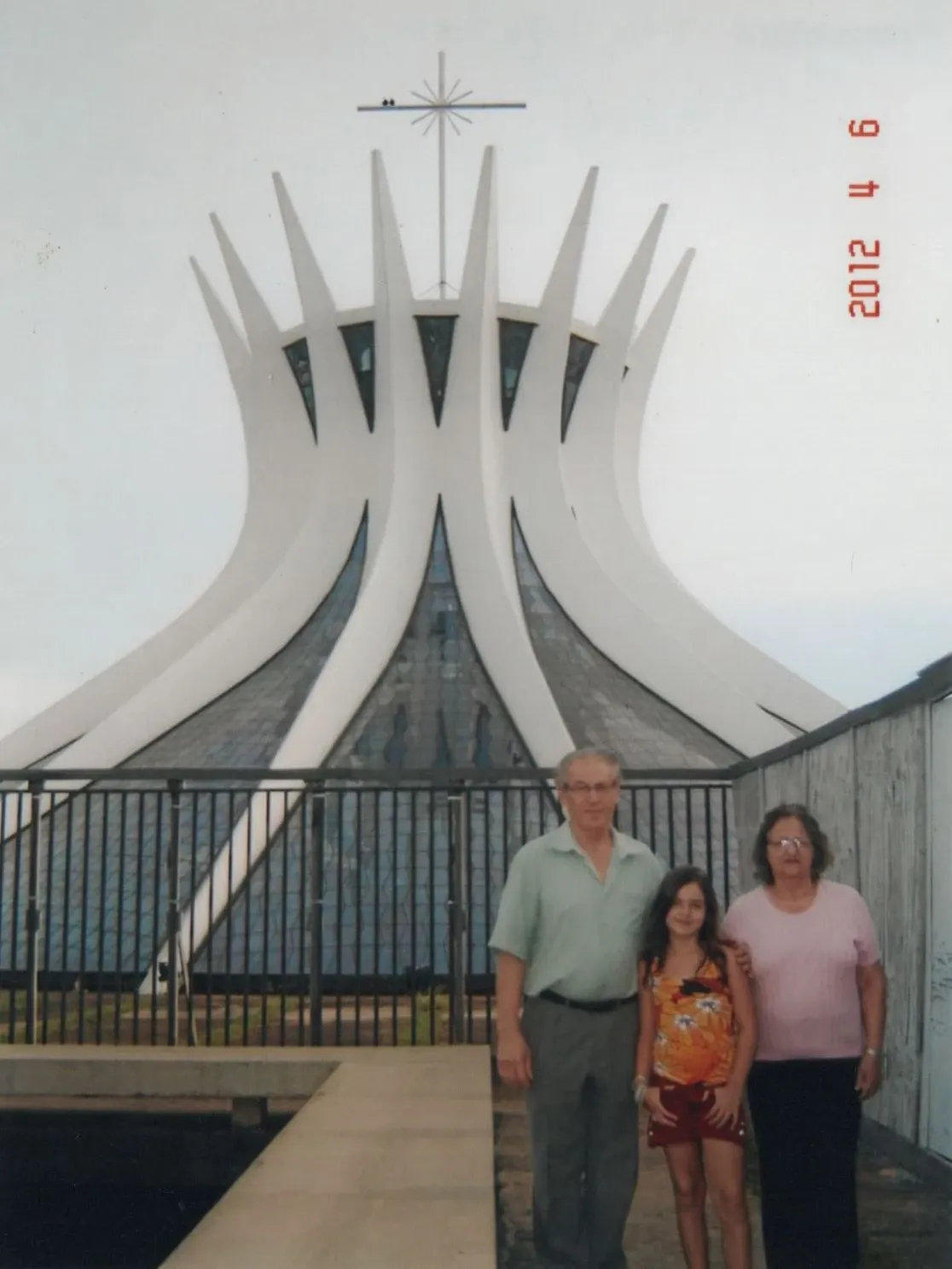 Uma jovem, um homem e uma mulher posam em frente à Catedral Metropolitana de Brasília.