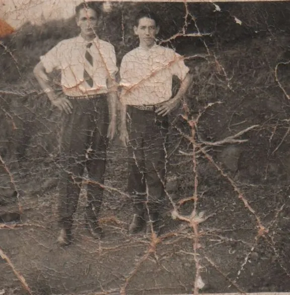 Dois homens em pé em uma trilha de terra entre a folhagem. (Original)