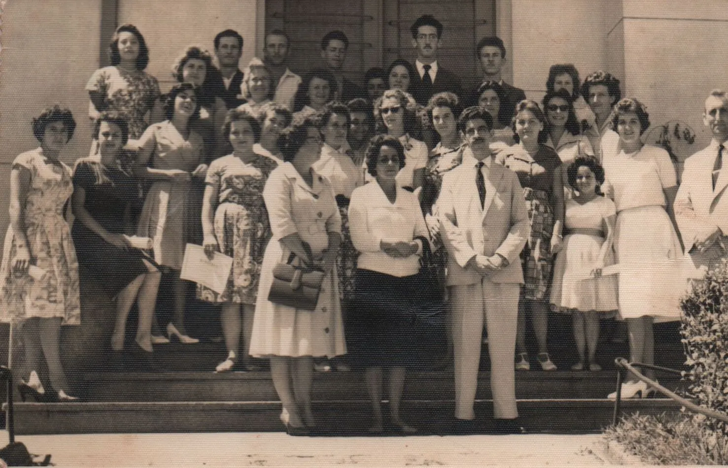 Grupo de homens e mulheres latinos elegantemente vestidos, a maioria deles jovens, posando em degraus ao ar livre. (Original)
