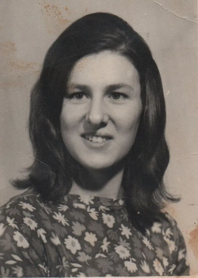 Uma mulher jovem com cabelo castanho escuro na altura dos ombros e um sorriso suave, vestindo uma blusa floral colorida. (Original)