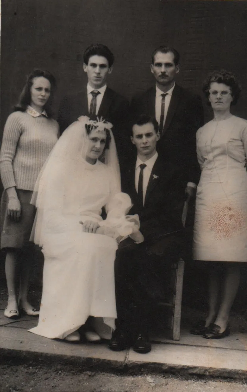 Uma foto de casamento vintage apresenta uma noiva e um noivo sentados, acompanhados por duas mulheres e dois homens em pé, todos olhando para a câmera. (Original)