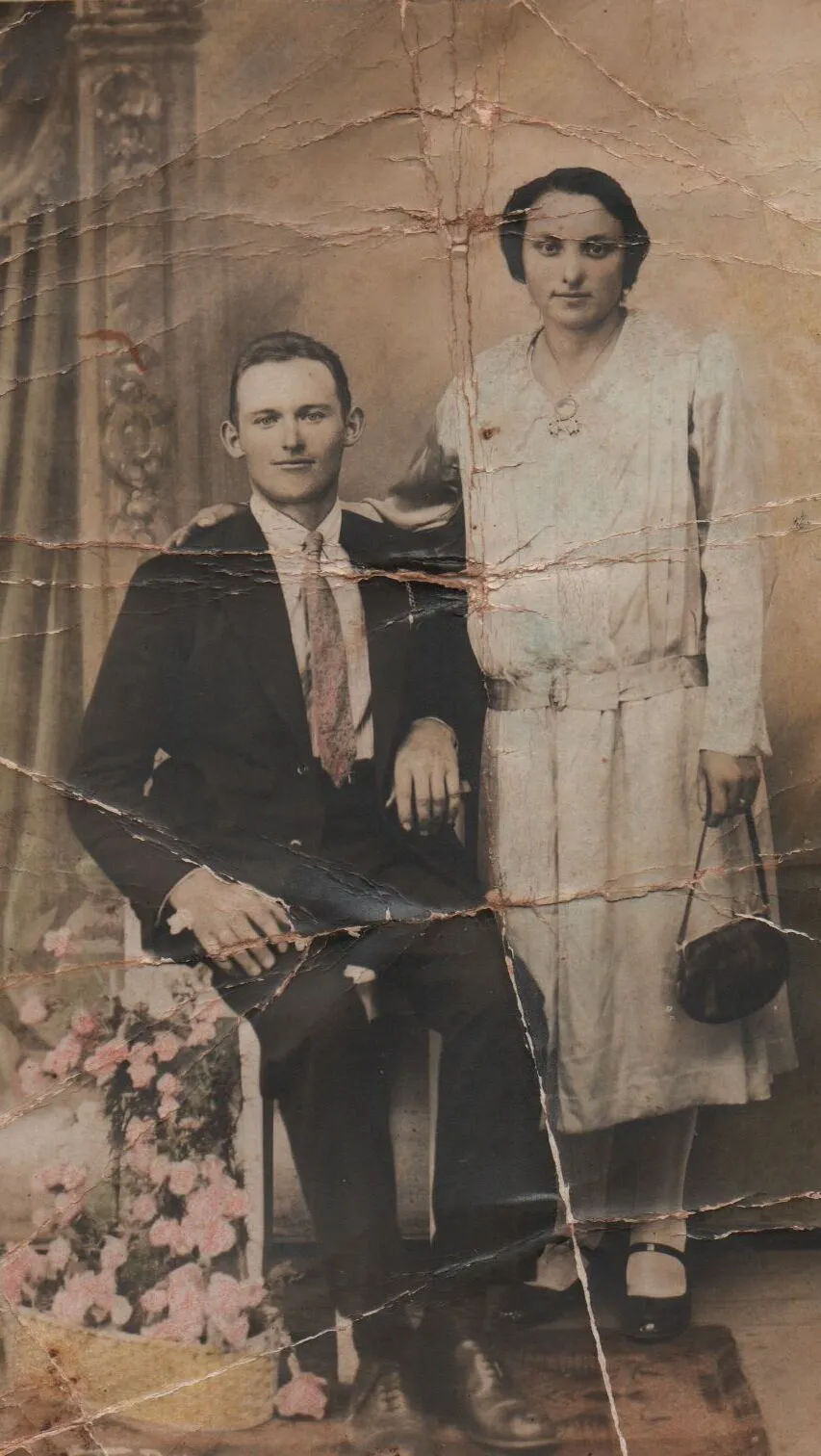 Casal posando para um retrato; a mulher está em pé e o homem está sentado. (Original)