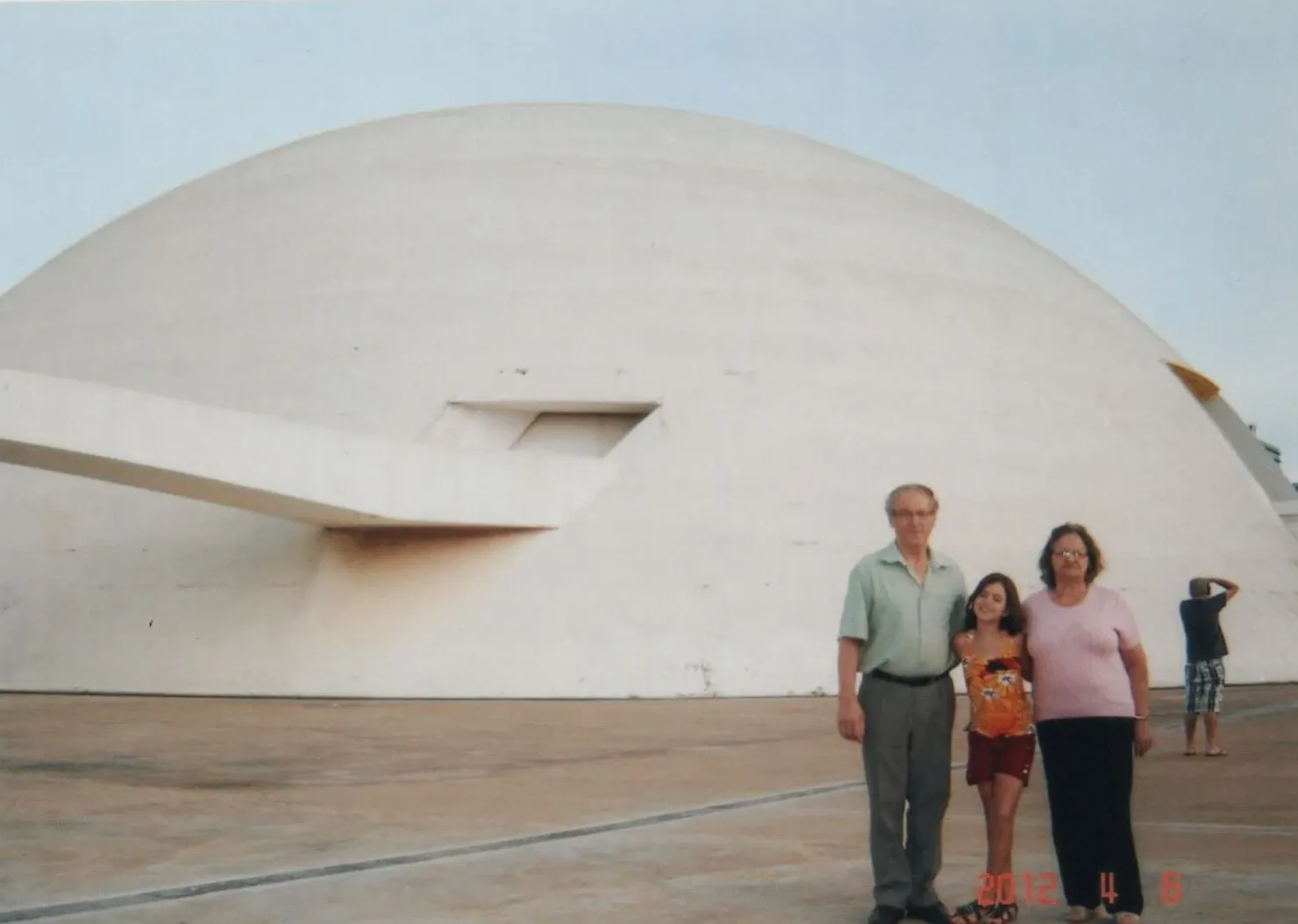 Duas mulheres e um homem posam na frente de uma estrutura em forma de domo com uma passarela que leva à entrada.