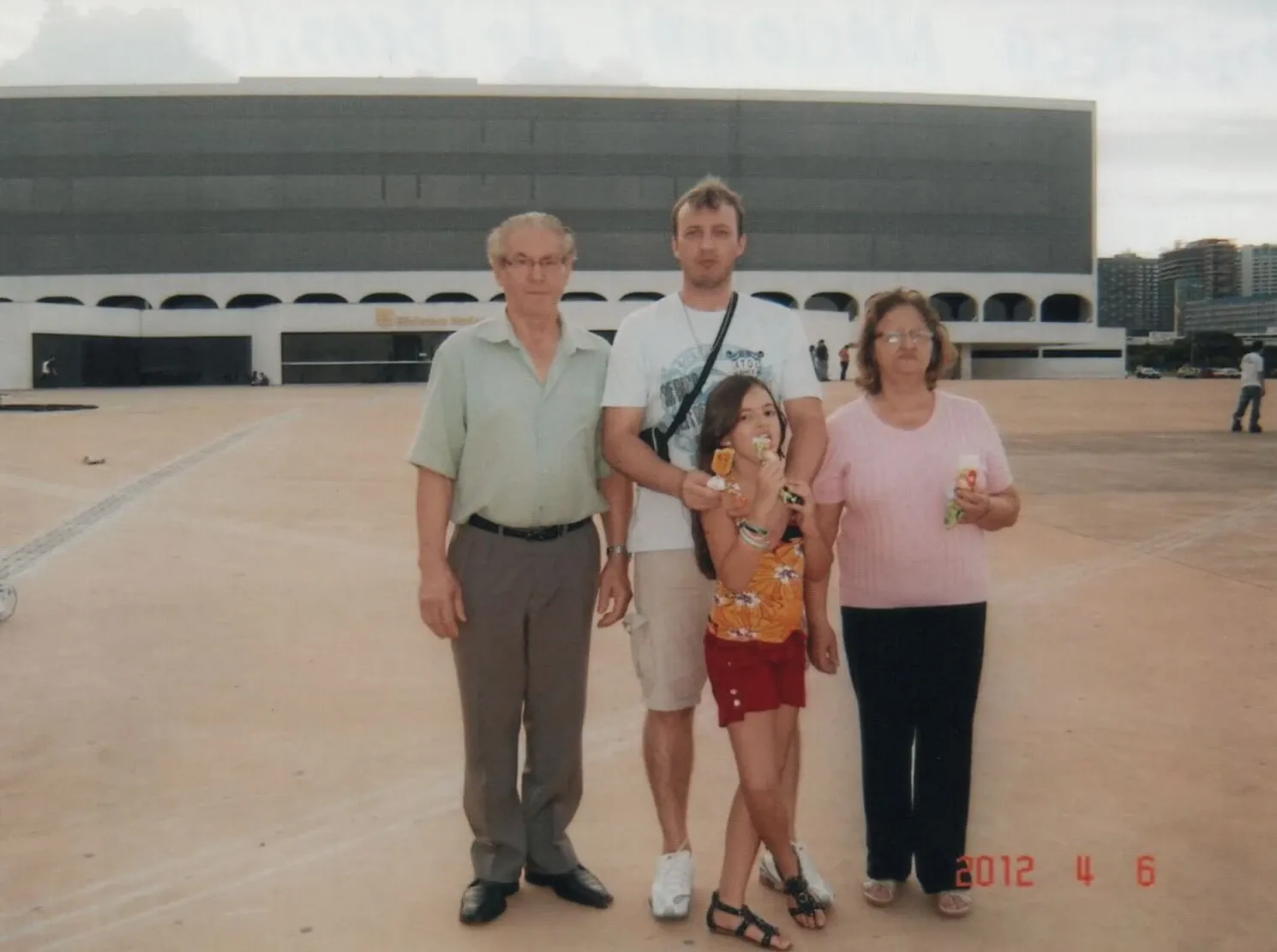 Uma família de quatro pessoas, incluindo um homem mais velho, um homem mais jovem, uma mulher e uma menina, posa ao ar livre.