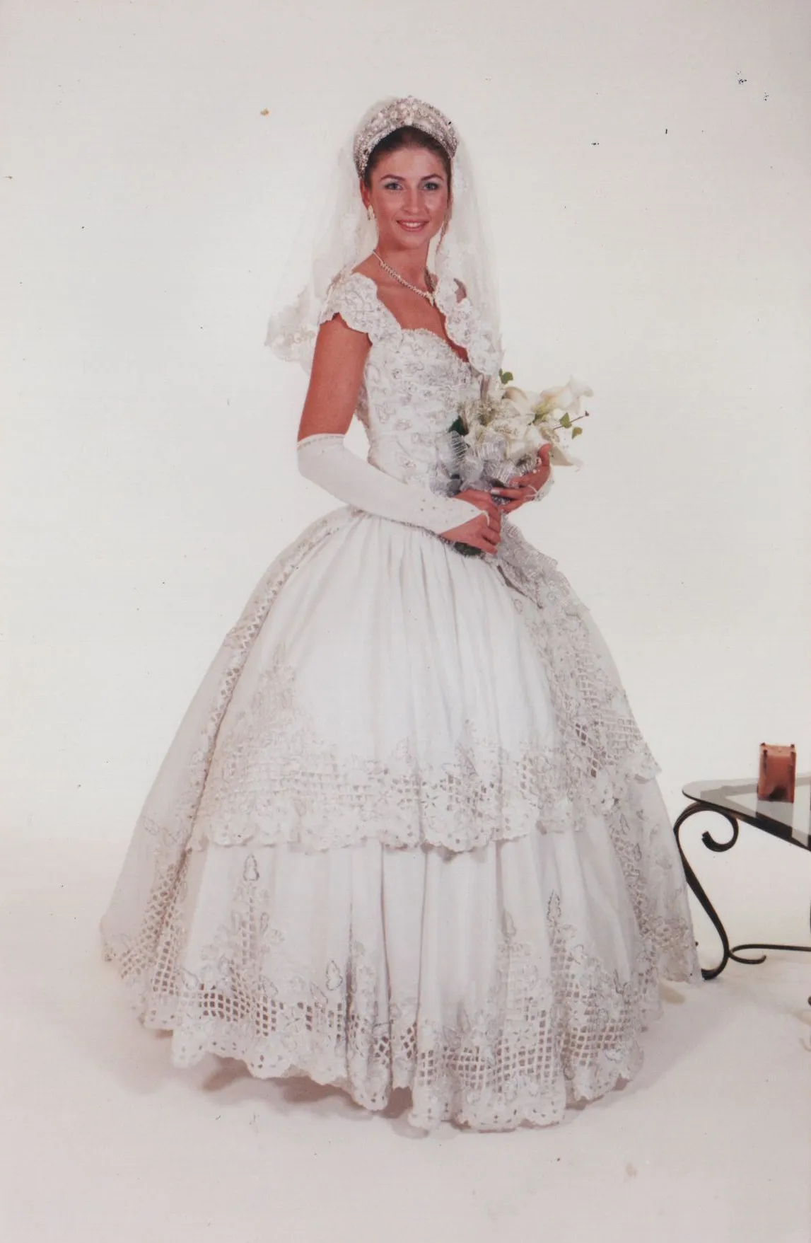 Noiva sorridente em um vestido de noiva branco tradicional, com véu e luvas brancas, segurando um buquê de flores brancas. (Original)