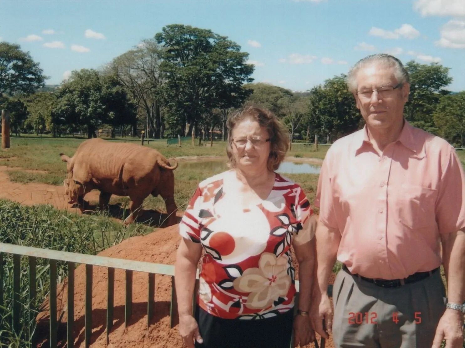 Casal de idosos em pé na frente de um rinoceronte em um habitat natural em um zoológico.