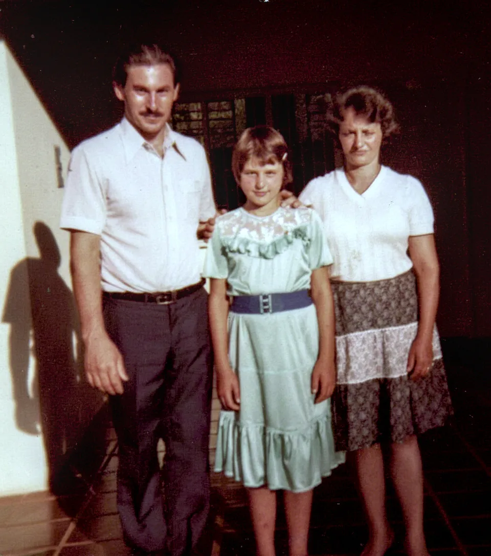 Um homem, uma mulher e uma criança em pé, o homem e a criança com os braços sobre os ombros um do outro.