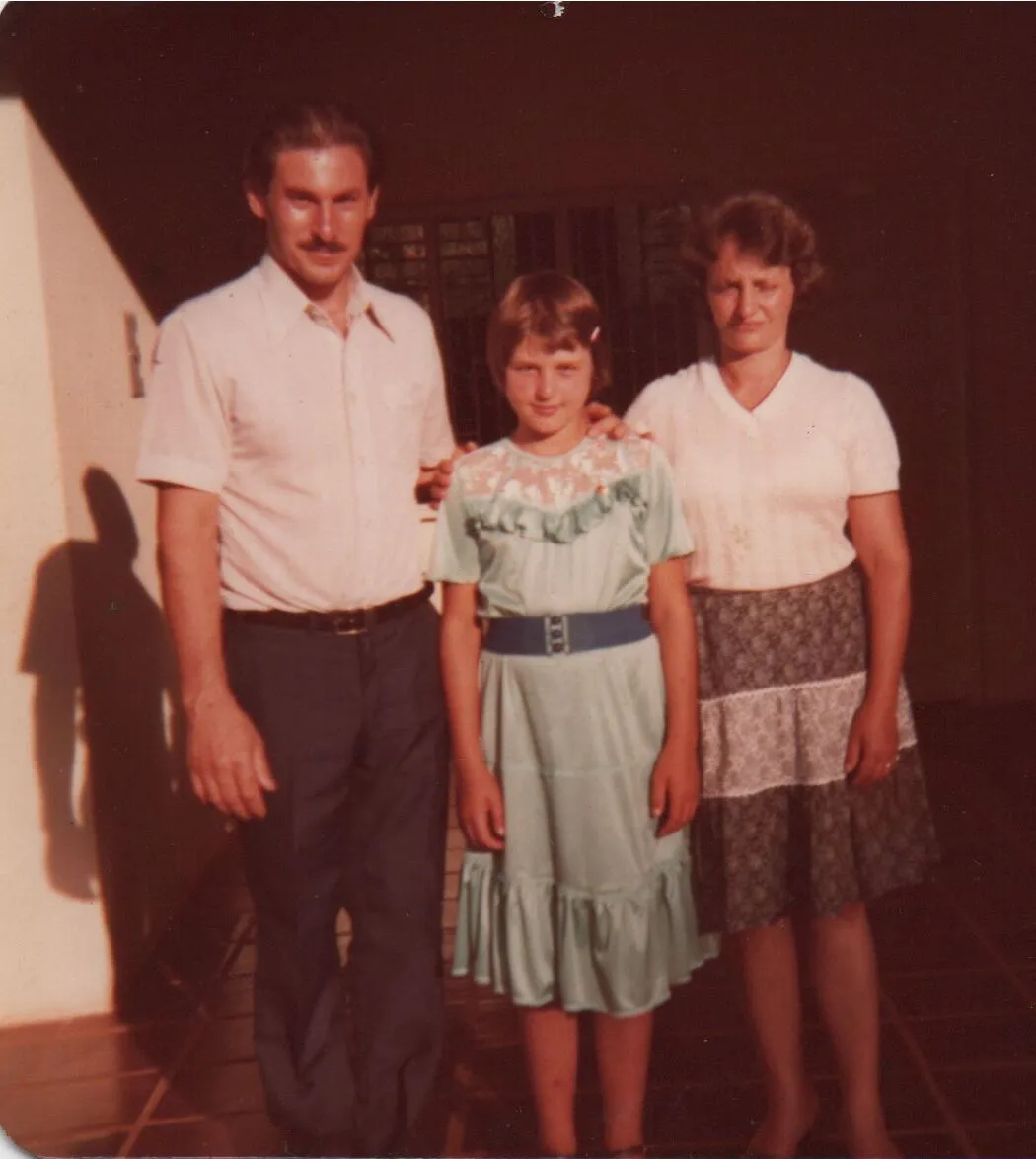 Um homem, uma mulher e uma criança em pé, o homem e a criança com os braços sobre os ombros um do outro. (Original)