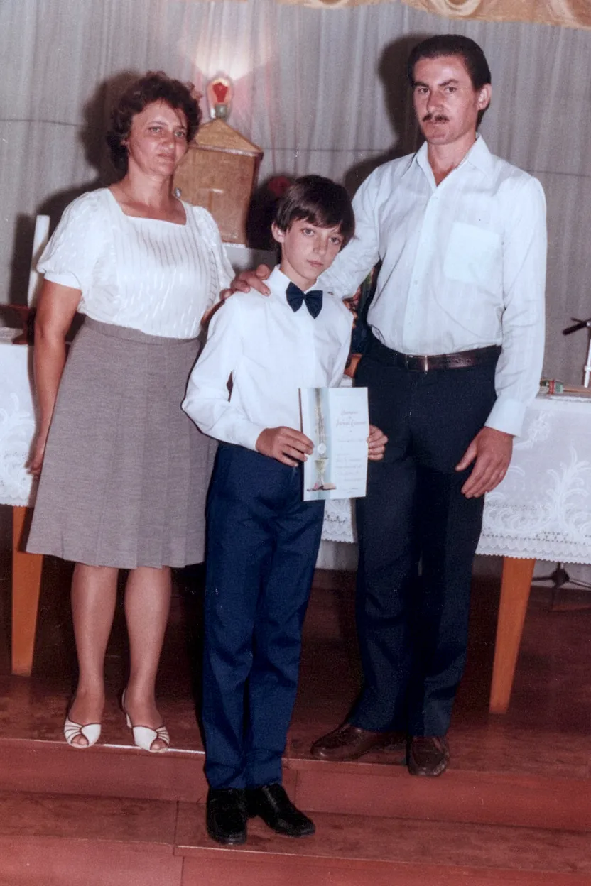 Um homem e uma mulher em roupas formais de pé com um menino em um smoking com uma gravata borboleta e um certificado.