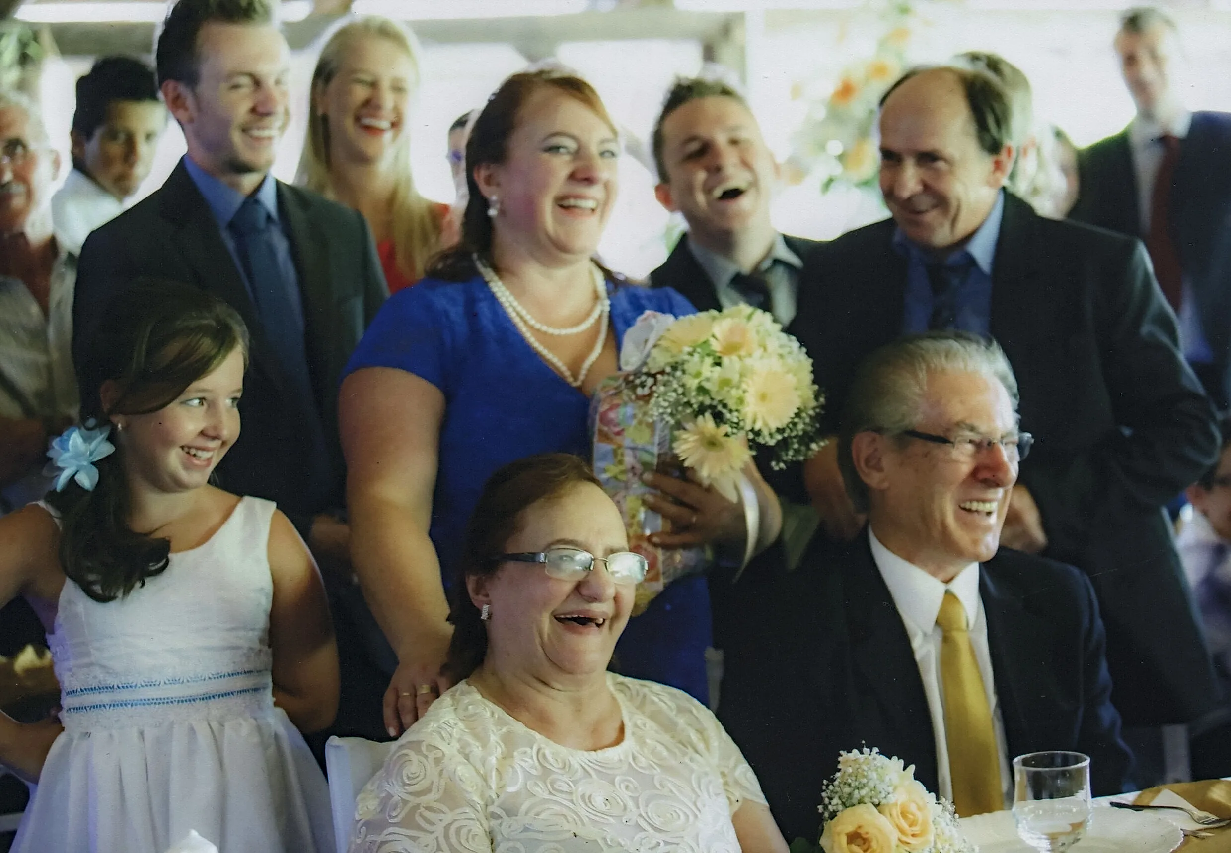 Um grupo de pessoas felizes se reúne em um evento, algumas sentadas e outras em pé, sorrindo e rindo.