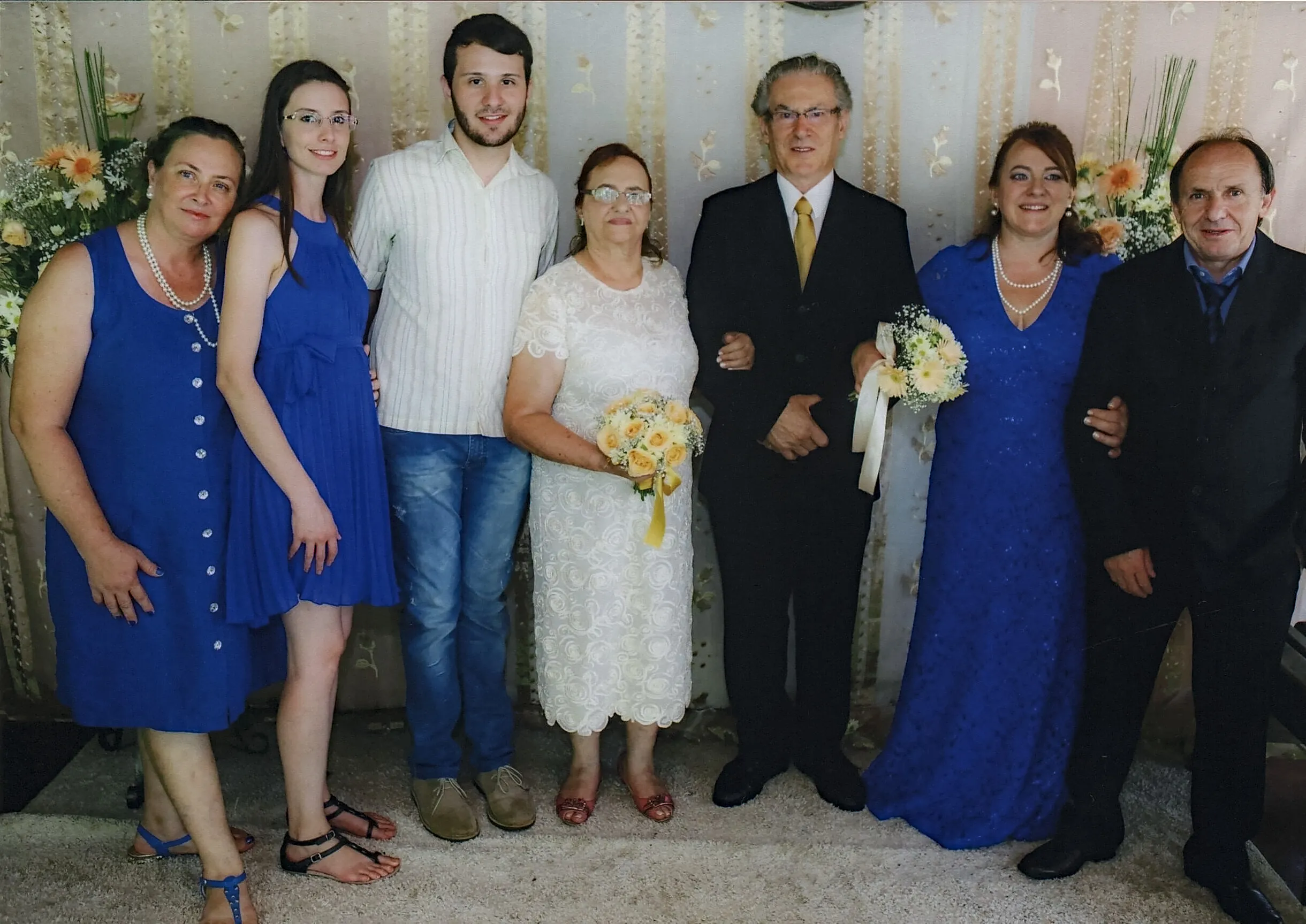 Sete pessoas, três homens e quatro mulheres, posam para uma foto em um casamento.