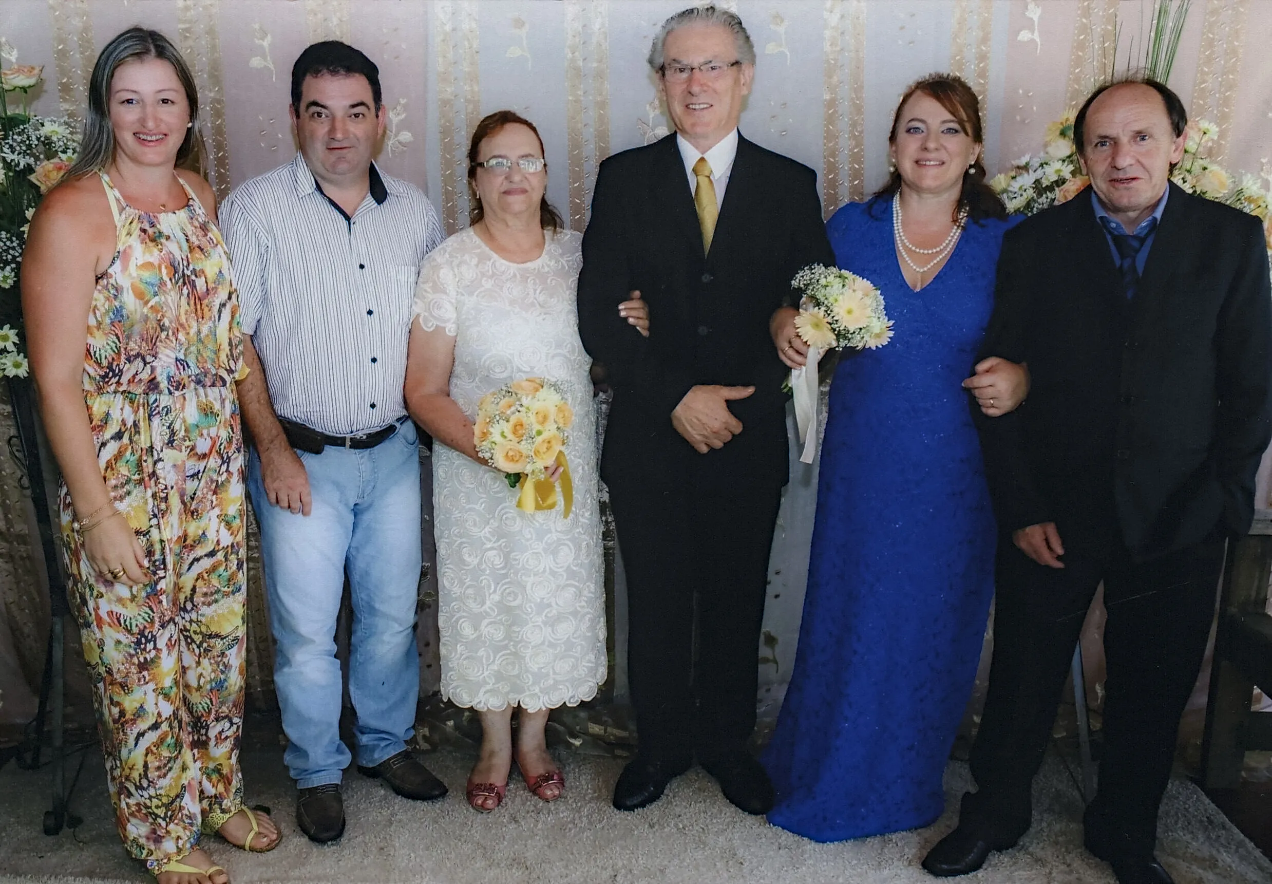 Seis pessoas, incluindo dois casais, posam para uma foto em um casamento.