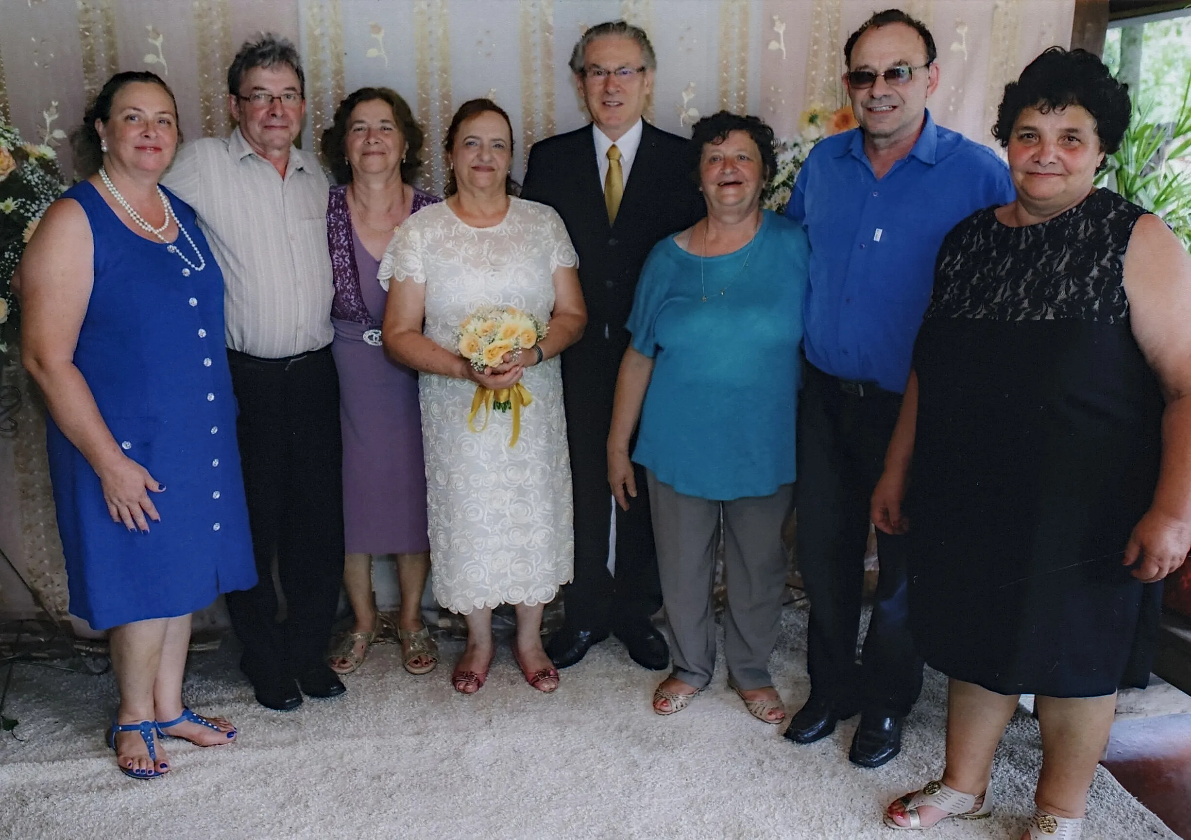 Um grupo de oito pessoas, três homens e cinco mulheres, estão posando para uma foto dentro de casa em um evento formal.
